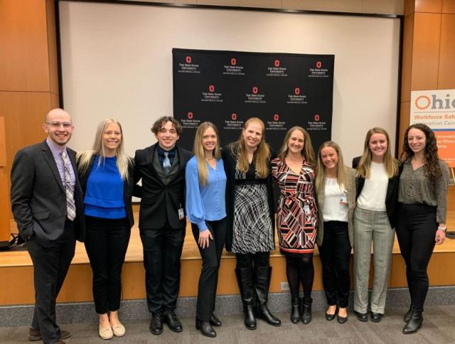 A group of nine people smiling in front of a black Ohio State University Wexner Medical Center backdrop.